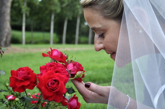 Femme en robe de mariée admire des roses rouges dans un jardin.
