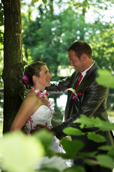 Un couple souriant en tenue de mariage, entouré de verdure.
