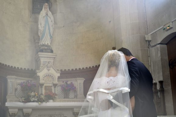 Un couple se penche l'un vers l'autre devant une statue de la Vierge, dans une église.